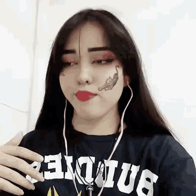 a woman with a tattoo on her face is wearing headphones and a t-shirt .