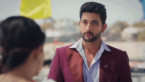 a man with a beard is wearing a maroon suit and a white shirt