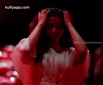 a woman in a white dress is standing in a dark room holding her hair .