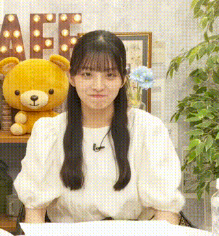 a girl in a white shirt is sitting at a table with a teddy bear behind her .