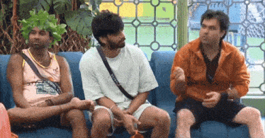 three men are sitting on a couch talking to each other . one of the men is wearing a basketball jersey .