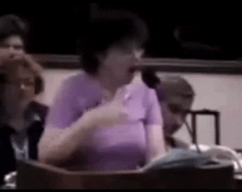 a woman in a purple shirt is giving a speech at a podium in front of a microphone .