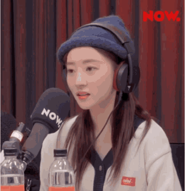 a woman wearing headphones and a blue hat is sitting in front of a microphone .