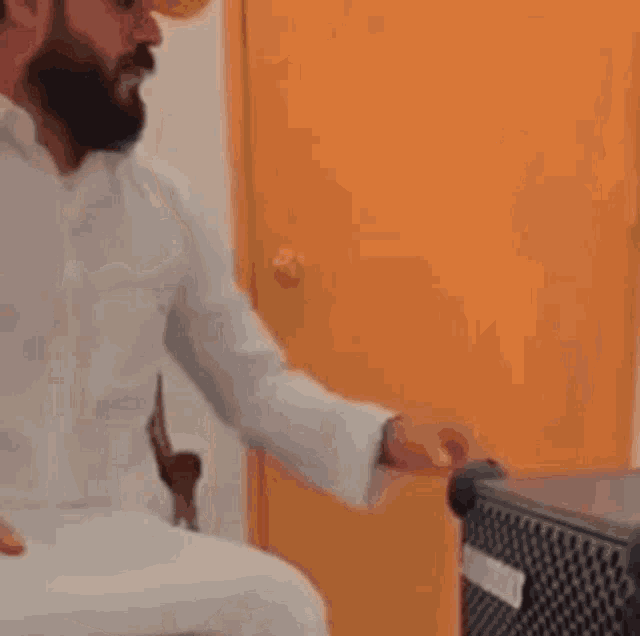 a man in a white robe and head scarf is sitting in a chair talking to another man .