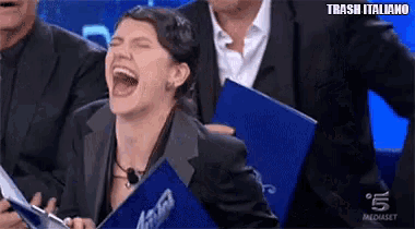 a woman in a suit is laughing while holding a blue folder with the words trash italiano on it .
