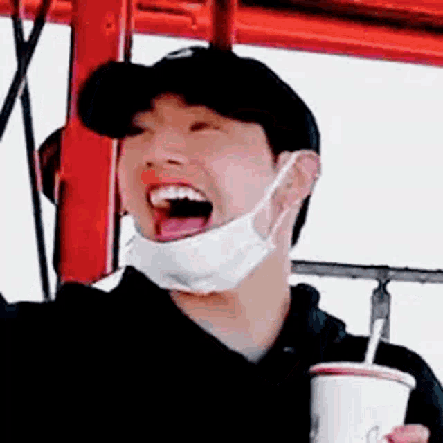a man wearing a mask and a hat is holding a cup of soda .