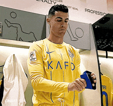 a man in a yellow kafd shirt holds a cell phone in a locker room
