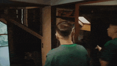 a man in a green shirt is standing in a closet looking at his phone .