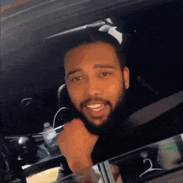 a man with a beard is sitting in a car with a bottle of water next to him