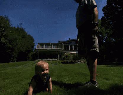 a little girl crawling in the grass with a man behind her