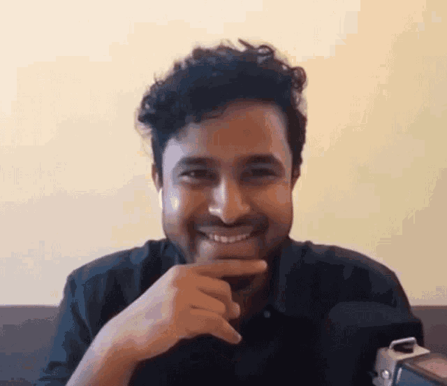 a man with curly hair is sitting on a couch with his hand on his chin and smiling .