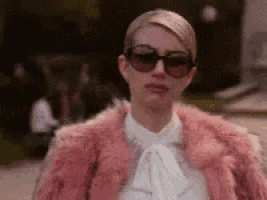 a woman wearing a pink fur coat and sunglasses is standing on a sidewalk .