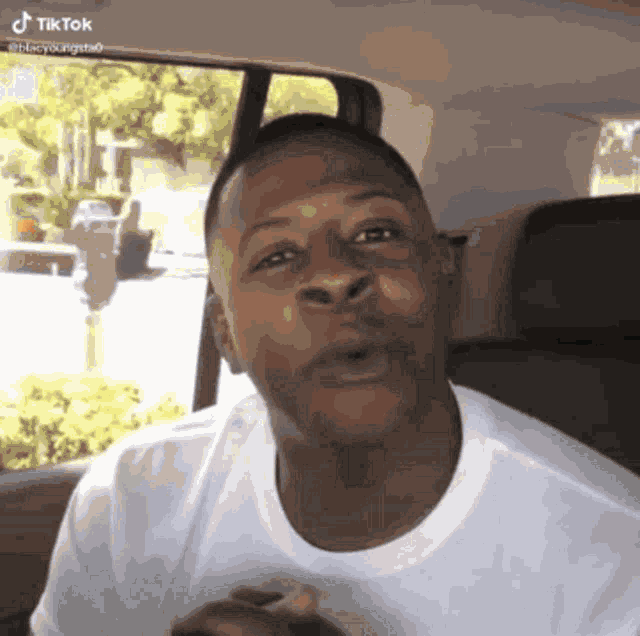 a man in a white shirt is sitting in the back seat of a car and talking