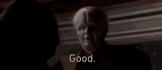 a man in a red robe is talking to another man in a dark room and saying `` good '' .