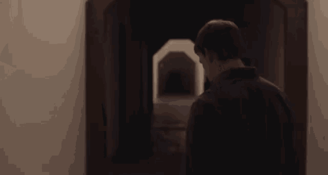 a man in a black shirt is standing in a dark hallway looking at himself in a mirror .
