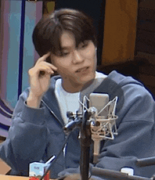 a man in a blue hoodie is sitting in front of a microphone and thinking .