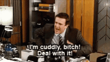 a man in a suit and tie is sitting at a desk saying i 'm cuddly bitch deal with it !