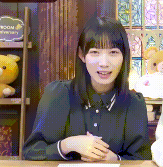 a young woman is sitting at a table with her hands folded in front of a teddy bear .