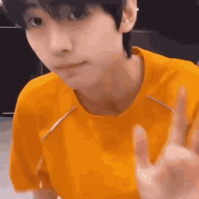 a close up of a person wearing an orange shirt giving the peace sign .