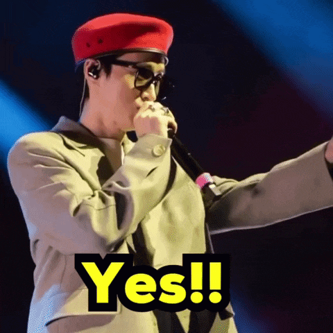a man wearing a red hat and glasses is singing into a microphone and the word yes is above him