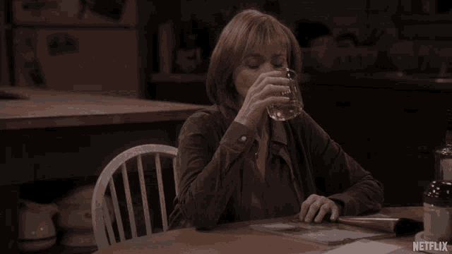 a woman sits at a table with a glass of water and a netflix logo on the table