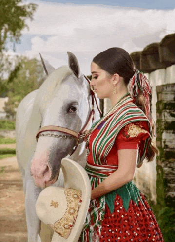 a woman in a red green and white dress stands next to a horse