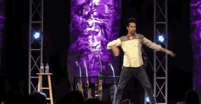 a man in a white shirt is dancing on a stage in front of a purple background