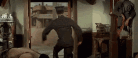 a man in a military uniform is standing in a room with a man laying on the floor .