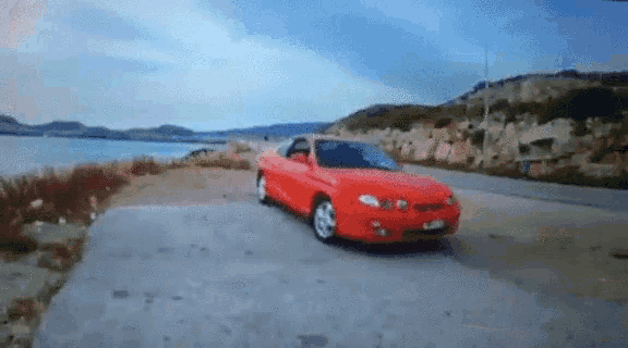 a red car is parked on the side of a road near a body of water