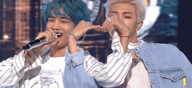 two men singing into microphones one with blue hair
