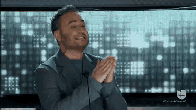 a man in a suit is clapping his hands while sitting in front of a screen .