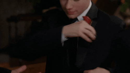 a man in a tuxedo has a red flower in his lapel