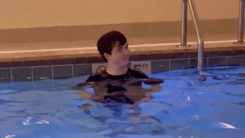 a man in a black shirt is swimming in a pool with a sign on the side that says " no diving "