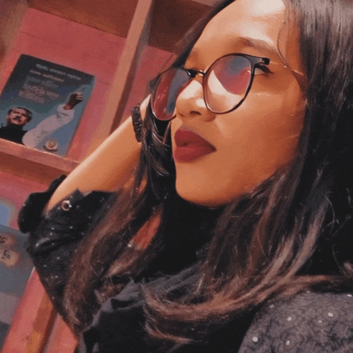 a woman wearing glasses stands in front of a shelf with a book on it that says ' a man '