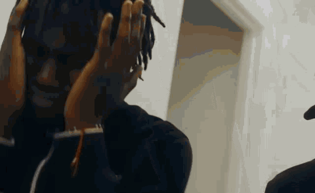 a man with dreadlocks is covering his ears with his hands while standing in a room .