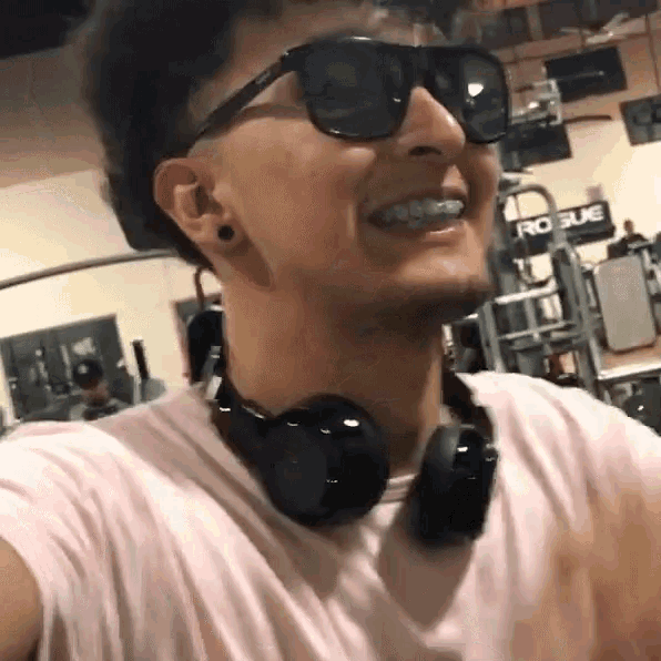 a man wearing headphones and sunglasses is smiling in a gym