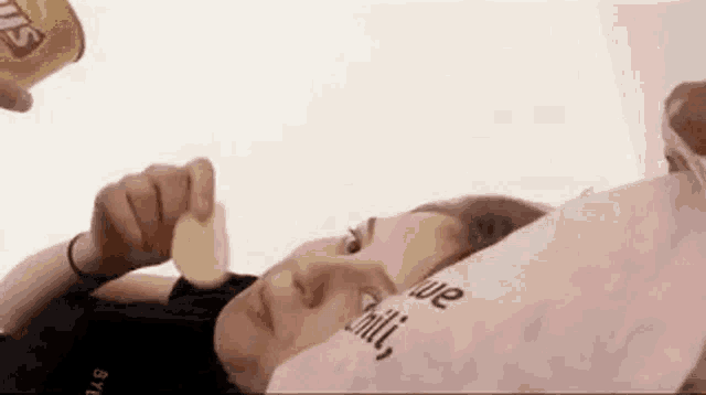 a woman is laying on a bed eating a potato chip while a man pours a can of chips on her head .