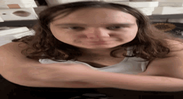 a close up of a young girl 's face with a white tank top on