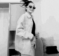 a black and white photo of a woman wearing sunglasses and a white jacket .
