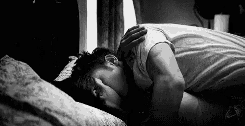 a man and a woman are laying in bed and the woman is kissing the man on the forehead .