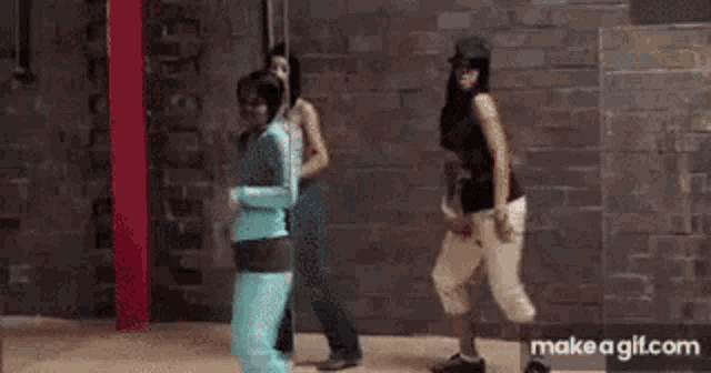 three women are standing next to each other in front of a brick wall in a room .