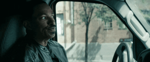 a man with a mustache is sitting in the driver 's seat of a vehicle