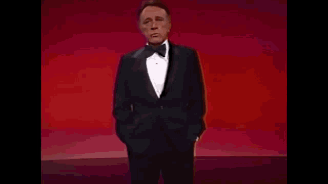 a man in a tuxedo is standing with his hands in his pockets