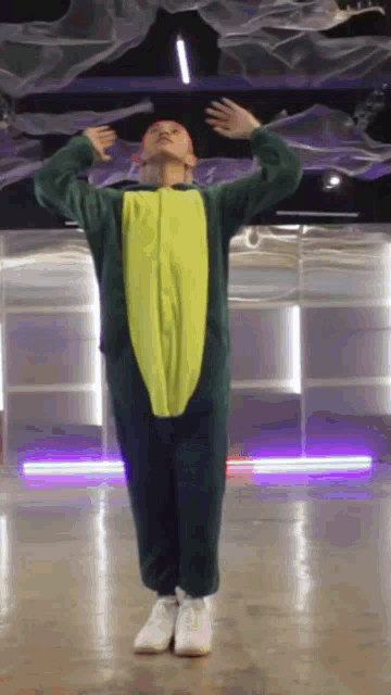 a man in a green and yellow dinosaur costume is dancing in a room .