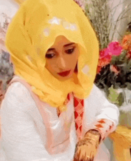 a woman wearing a yellow hijab and a white shirt is sitting on a chair .