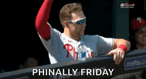 a man in a phillies jersey is standing in the dugout with his arms in the air .