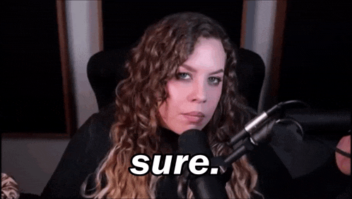 a woman with curly hair is sitting in front of a microphone and saying `` sure '' .
