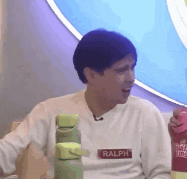 a man wearing a white sweater with the name ralph on it is sitting at a table holding a bottle .