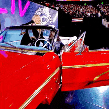 a man and a woman are in a red car with the word dogmen on the wall behind them