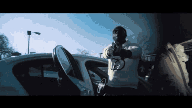 a man holding a gun in front of a car with a hoodie that has the letter n on it